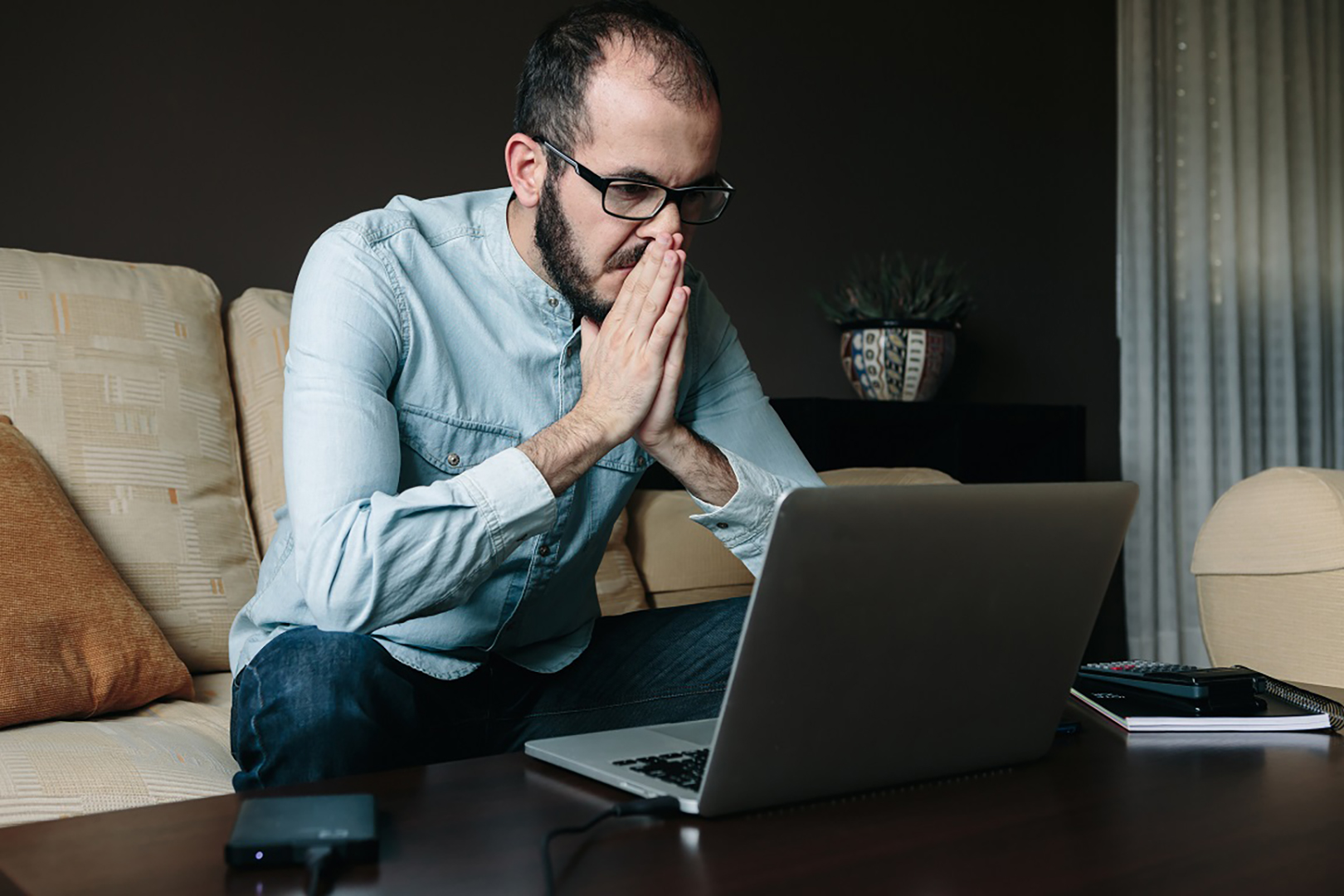 Worried man reading bad news on the laptop computer while working remotely at home. Telecommuting, telework and teleworking concept. 